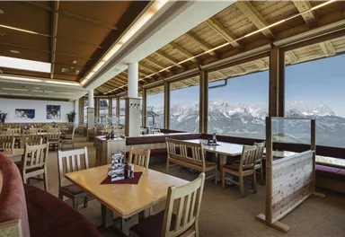 Ein gemütliches Restaurant mit großen Fenstern und Blick auf die Berge. Die Tische sind ordentlich gedeckt und es gibt eine angenehme, einladende Atmosphäre.