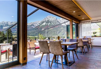 A cozy restaurant scene with tables and chairs that offers a stunning view of the mountains. Large windows let in plenty of natural light.