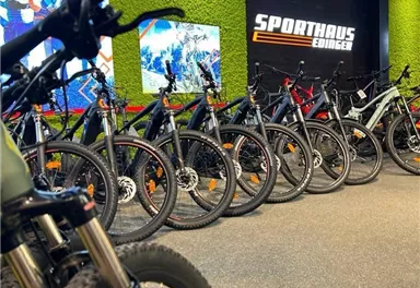 Ein modernes Geschäft mit vielen Mountainbikes in einer Reihe. Im Hintergrund sind ansprechende Grafiken und das Logo "Sporthaus" zu sehen.