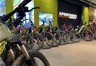 Eine Auswahl von Mountainbikes in einem Sportgeschäft. Im Hintergrund ist das Logo von "Sporthaus Edinger" zu sehen.