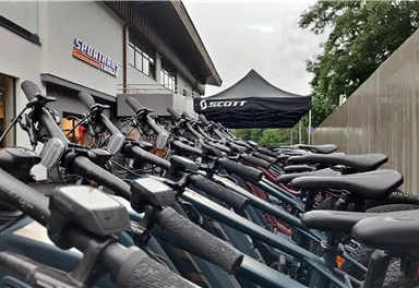 Eine Reihe von Fahrrädern steht vor einem Geschäft. Im Hintergrund ist ein Zelt zu sehen, das die Marke Scott präsentiert.