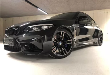 A sporty BMW in a modern parking garage. The car is black with eye-catching rims and a dynamic design.