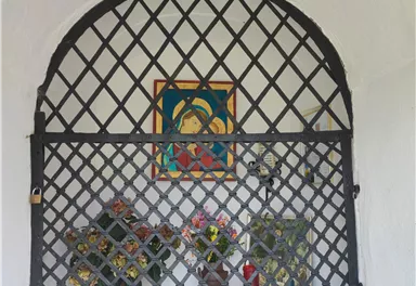 An adorned niche with a lattice, featuring a colorful picture and a floral arrangement. The niche appears peaceful and inviting.