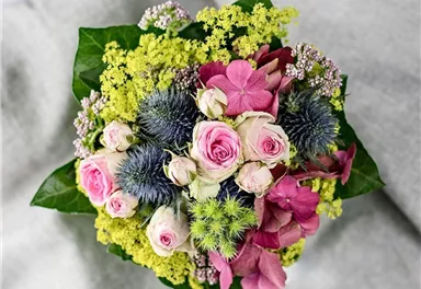 Ein bunter Blumenstrauß mit rosa und lila Blüten sowie grünen Akzenten. Die Blumen sind auf einem grauen Hintergrund angeordnet.