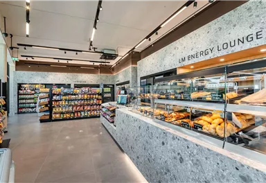 A modern sales room with shelves full of snacks and beverages. In the foreground, there is a selection of baked goods in a counter.