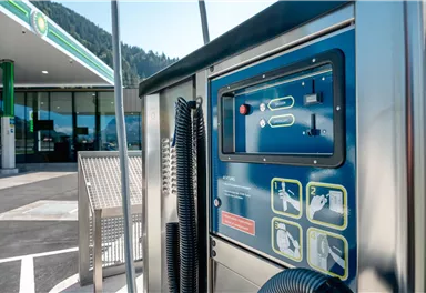 A modern gas station with a self-service kiosk. In the background, the gas station building is visible.