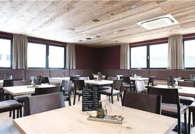 Ein modernes Restaurant mit hellen Holzmöbeln und großen Fenstern. Die Tische sind ordentlich gedeckt und der Raum wirkt einladend und geräumig.