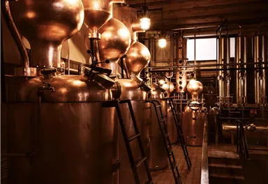 Eine Brennerei mit mehreren kupfernen Brennkolonnen. Das warme Licht schafft eine einladende Atmosphäre.