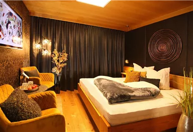 A modern bedroom with a large bed and stylish furniture. The walls are painted in warm tones, and a cozy seating area complements the space.