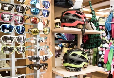 Eine Auswahl an Sonnenbrillen und Fahrradhelmen steht in einem Geschäft aus. Im Hintergrund sind verschiedene Accessoires sichtbar.