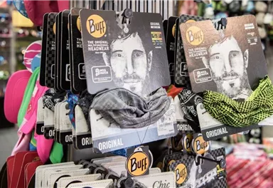 Eine Auswahl von Buff-Accessoires in verschiedenen Farben und Designs hängt im Geschäft. Die Produkte sind gut sortiert und zeigen unterschiedliche Muster.