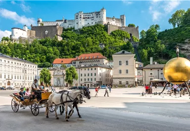 A beautiful spot in Salzburg with a horse-drawn carriage and historic architecture. In the background, one can see an impressive fortress on a hill.