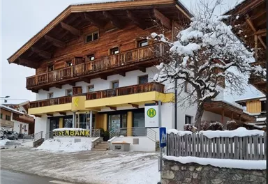 Ein traditionelles Gebäude mit Holzfassade und einem weißen Erdgeschoss. Draußen liegt Schnee, und es gibt eine Bank mit dem Schriftzug „Eisenbank“.
