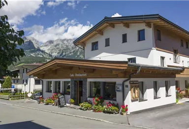 Ein gemütliches Restaurant mit einer schönen Holzveranda. Im Hintergrund sind die Berge und ein klarer blauer Himmel zu sehen.