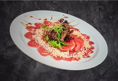 A plate with carpaccio, garnished with fresh salad and parmesan cheese. The presentation is elegant with a decorative sauce.