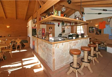 Eine gemütliche Bar mit Holzdekor und Steinhintergrund. Helle Lichtstrahlen fallen durch die Fenster und sorgen für eine einladende Atmosphäre.