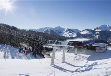 A wintry mountain landscape with snow-covered mountains and a gondola. The sky is clear and sunny.