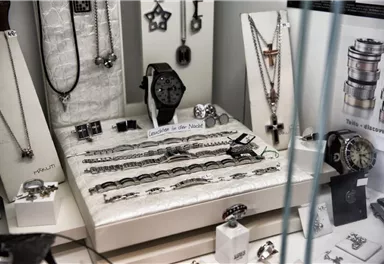 An elegant jewelry display case with various pieces of jewelry such as watches, necklaces, and bracelets. The showcase displays a variety of silver and black designs.