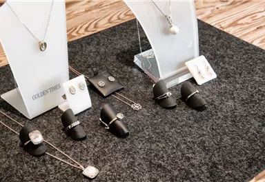 A stylish jewelry display with various necklaces, rings, and earrings. The jewelry pieces are placed on a dark background and stand out well.