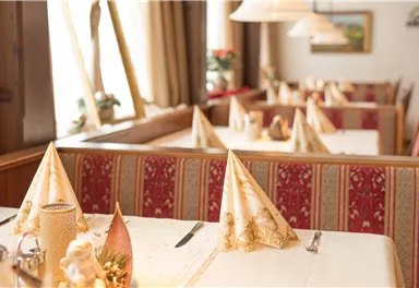 Ein eleganter Restaurantbereich mit festlich gedeckten Tischen. Die Tischdecken sind weiß, und die Servietten sind kunstvoll gefaltet.