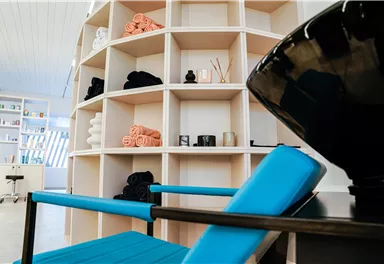 Ein modernes Lounge-Bereich mit einem blauen Stuhl und einem Regalsystem. Im Regal sind verschiedene Handtücher und Dekorationsartikel ordentlich angeordnet.