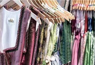 Eine Auswahl an traditionellen Kleidungsstücken hängt auf Kleiderbügeln. Die Farben reichen von Rosa bis Grün, mit feinen Details und Verzierungen.