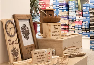 A sales display with decorative wooden objects stands in the foreground. In the background, shelves with colored shoe boxes are visible.
