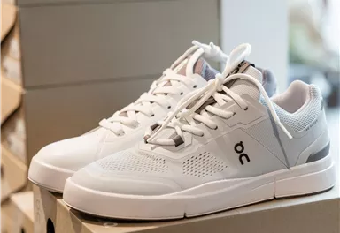 A pair of white sneakers on a stack of shoeboxes. The shoes have a modern design and are suitable for everyday wear.