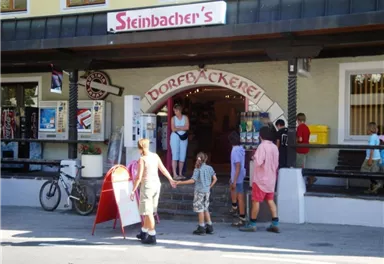 A traditional village bakery with an entrance that attracts guests. Children are standing nearby, waiting for their treats.