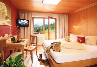 A cozy hotel room with a large bed and wooden walls. There is a balcony overlooking the landscape and a small seating area.