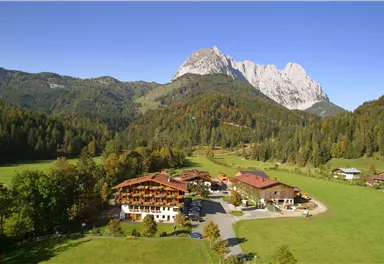 Eine malerische Landschaft mit einem großen Berg im Hintergrund. Im Vordergrund sind schöne Gebäude und grüne Wiesen.