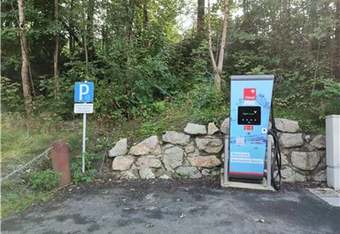 A charging station for electric cars in a forested area. Next to the station is a parking sign.
