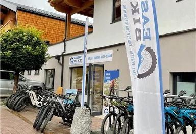 Ein Fahrradverleih mit mehreren Fahrrädern an einem geschäftigen Standort. Es gibt ein großes Banner mit der Aufschrift "Easy Bike".