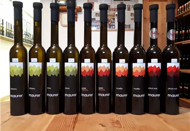 Eine Reihe von Flaschen mit Olivenöl steht auf einem Holztablett. Die Flaschen haben unterschiedliche Etiketten in verschiedenen Farben.