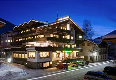 A charming hotel in the evening light, surrounded by snow-capped mountains. The warm lights from the windows create an inviting atmosphere.