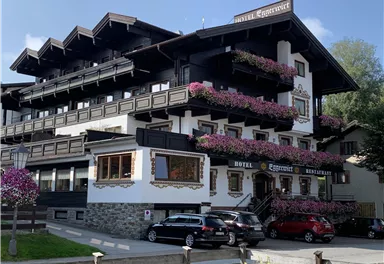 Ein charmantes Hotel mit traditionellen Holzdetails und bunten Blumenkästen. Die Fassade ist hell und einladend, umgeben von einem Parkplatz.