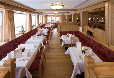 An elegant restaurant with wooden furniture and white tablecloths. Large windows provide plenty of daylight and an inviting atmosphere.