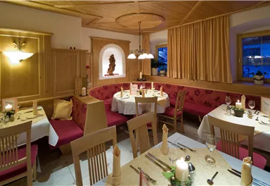 A cozy restaurant with wooden paneling and red benches. The tables are elegantly set with candles and cutlery.