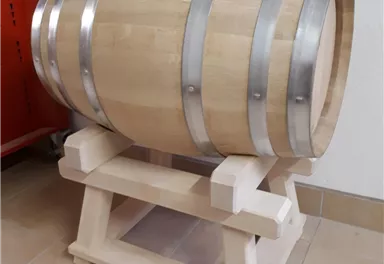 Ein kleines Holzfass auf einem stabilen Ständer. Es hat Metallbeschläge und steht auf einem hellen Boden.