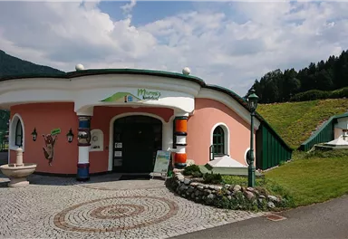 A colorful building with a round shape and an inviting door. In the background, gentle hills and trees can be seen.