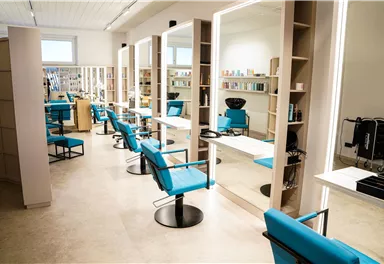 Ein moderner Friseursalon mit blauen Stühlen und großen Spiegeln. Regale mit Haarpflegeprodukten sind im Hintergrund sichtbar.