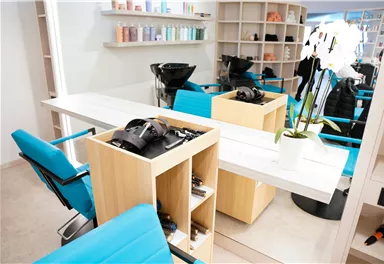 Ein moderner Friseursalon mit hellblauen Stühlen und einer stilvollen Einrichtung. Auf den Regalen sind verschiedene Haarpflegeprodukte sichtbar.