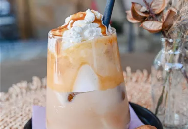 Ein köstliches Kaltgetränk mit Sahne und Caramel auf Eis. Dazu liegt ein Keks auf einem schwarzen Teller.