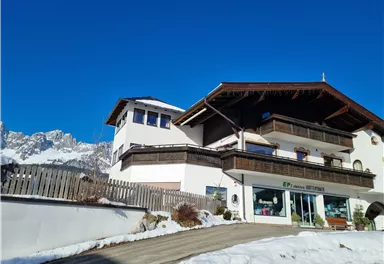 A charming Alpine house with multiple floors. The sky is clear and blue, and there is snow on the ground.