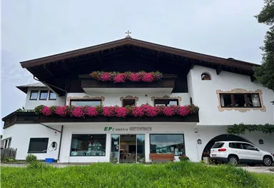 A charming house with traditional architecture, adorned with colorful flowers. In the foreground, a car is parked, surrounded by a green meadow.