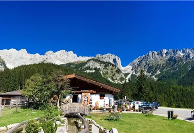 A cozy building in the mountains with a beautiful landscape. In the background, majestic mountains and a clear blue sky can be seen.
