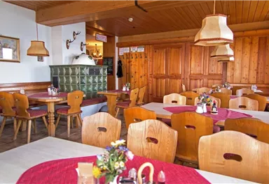 Ein gemütliches Restaurant mit Holzmöbeln und einem rustikalen Ambiente. Die Tische sind mit roten Tischdecken und Blumen dekoriert.