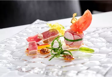 Ein elegantes Gericht mit frisch zubereitetem Fisch, Garnele und Gemüse. Es ist kunstvoll auf einem gläsernen Teller angerichtet.