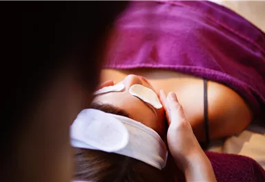 Eine Person erhält eine Gesichtsbehandlung mit Augenpads. Die Umgebung ist entspannend und freundlich.