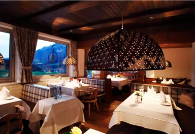 Ein stilvolles Restaurant mit eleganter Beleuchtung und Tischen, die für Gäste vorbereitet sind. Im Hintergrund ist eine malerische Landschaft zu sehen.